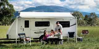 Family sitting eating lunch outside caravan in a field