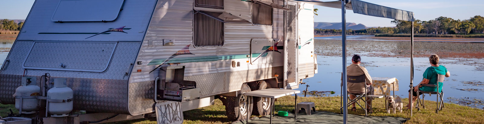 Couple sitting outside their caravan with a lake setting